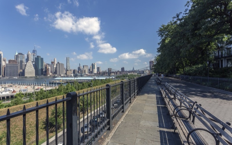 Stone-paved Brooklyn Heights Promenade with benches, trees and the Lower Manhattan skyline across the East River